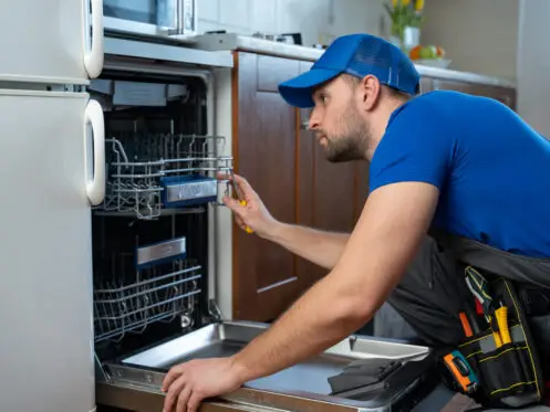 Repair of dishwashers. Repairman repairing dishwasher in kitchen.