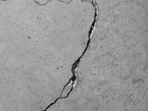 Closeup detail of a weathered cement floor with diagonal cracks.